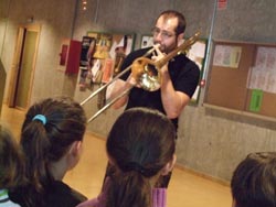 Un músico toca o trombón mentras os nenos escoitan