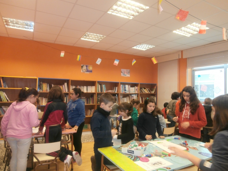 Nenos e nenas facendo traballos plásticos en grupos na biblioteca