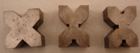 Calzos para apoyo de piezas. Se ven tres piezas macizas con forma de X pero con distintos ángulos para apoyar y  sujetar distintos tipos de piezas.